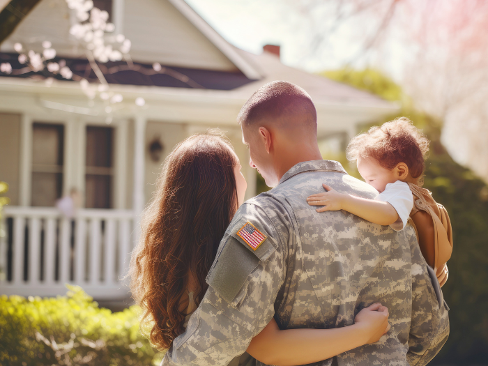 Veterano estadounidense sosteniendo a su familia mientras se encuentra frente a una nueva casa.