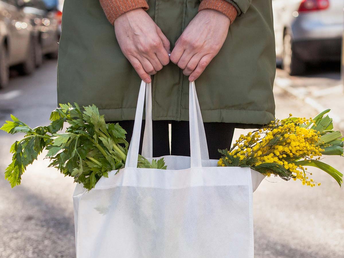 Horizontal - A woman standing in the street with focus on a bag of vegetables and flowers