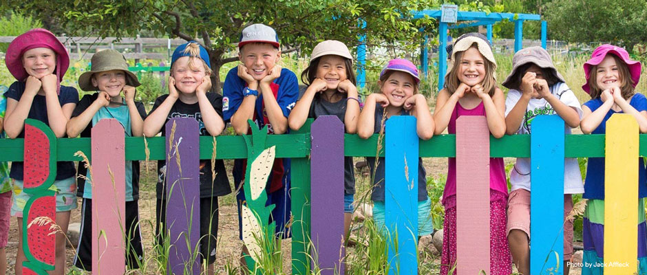 Children smiling leaning on a colorful painted fence in front of a playground