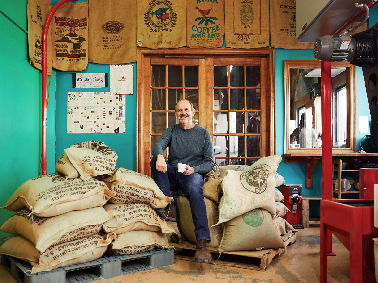 The owner of Conscious Coffees sitting on a stack of burlap bags of coffee beans