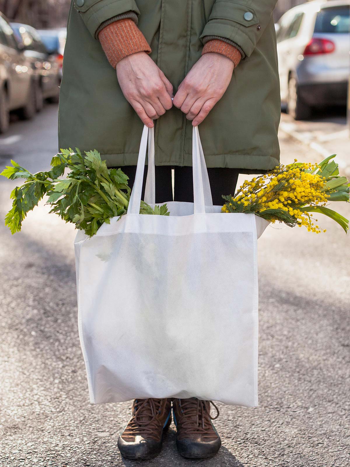 A woman standing in the street with focus on a bag of vegetables and flowers