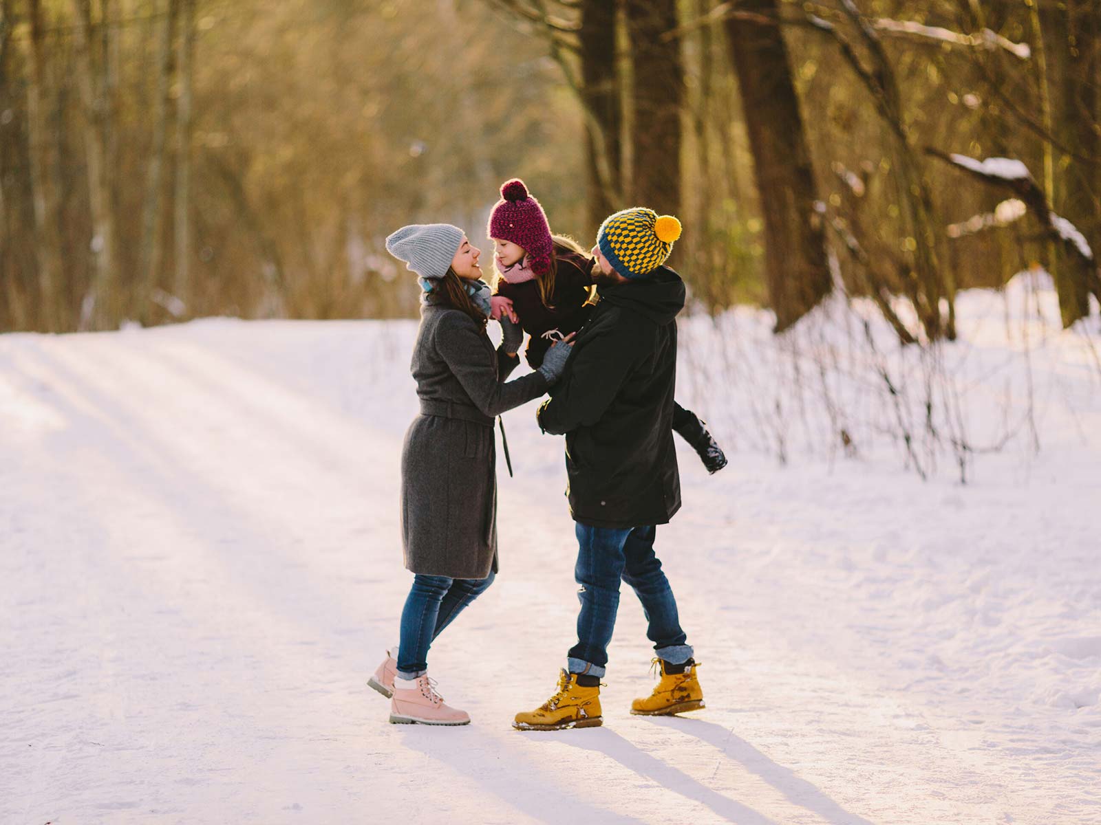 Daughter in purple winter hat being passed from Dad to Mom in a winter forest