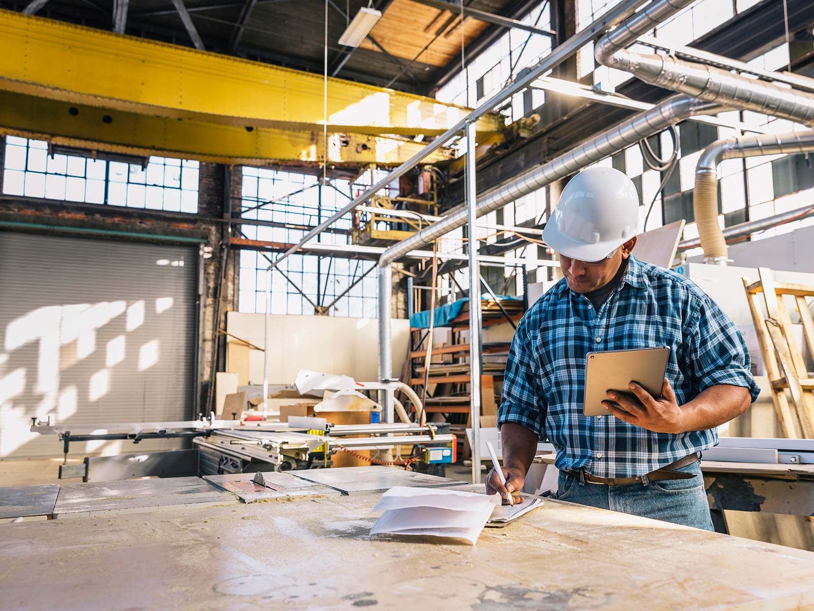 Man in hardhat reviewing orders on a clipboard in a warehouse