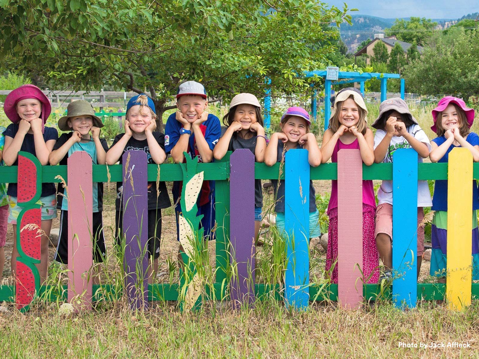 Niños sonriendo apoyados en una colorida valla pintada frente a un patio de recreo