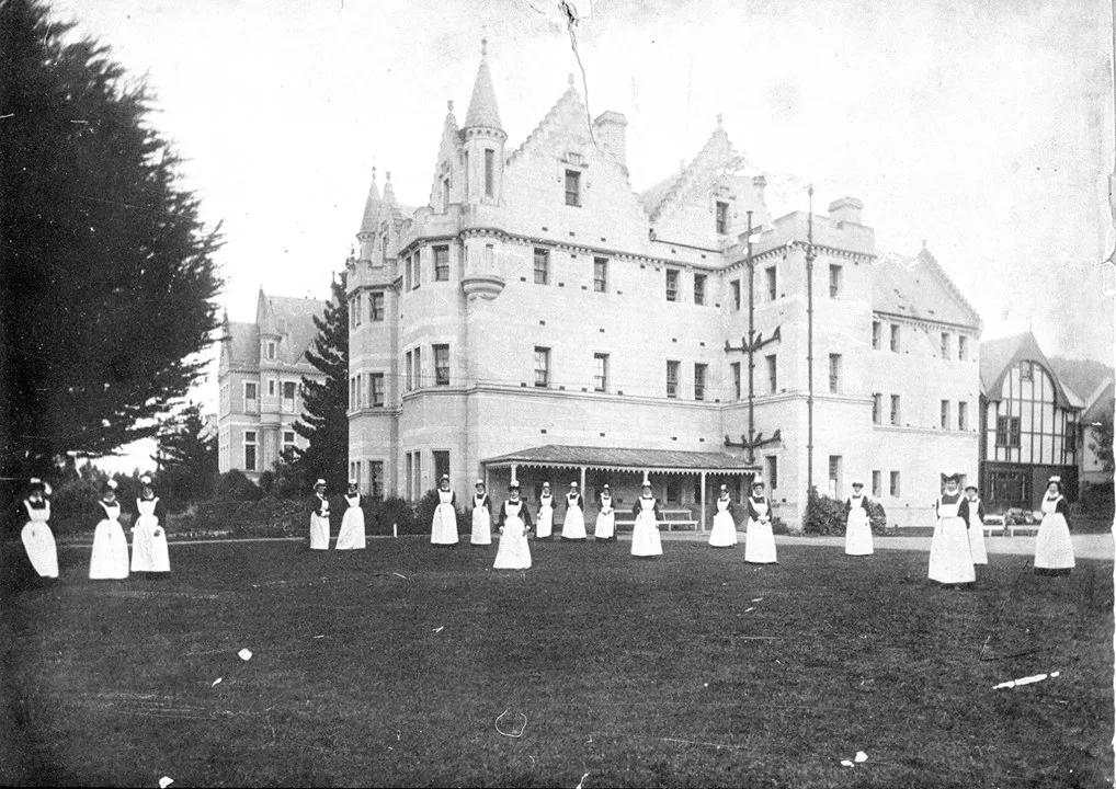 Black and white photograph of a large building and grounds with nurses standing around looking at the camera