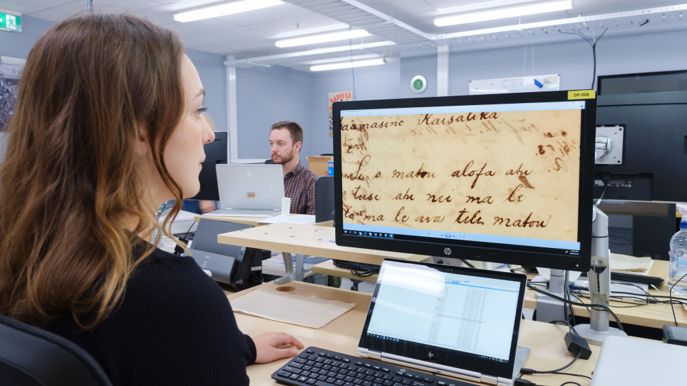 A staff member digitises a German Sāmoan record A woman views a scan of an old record on a computer