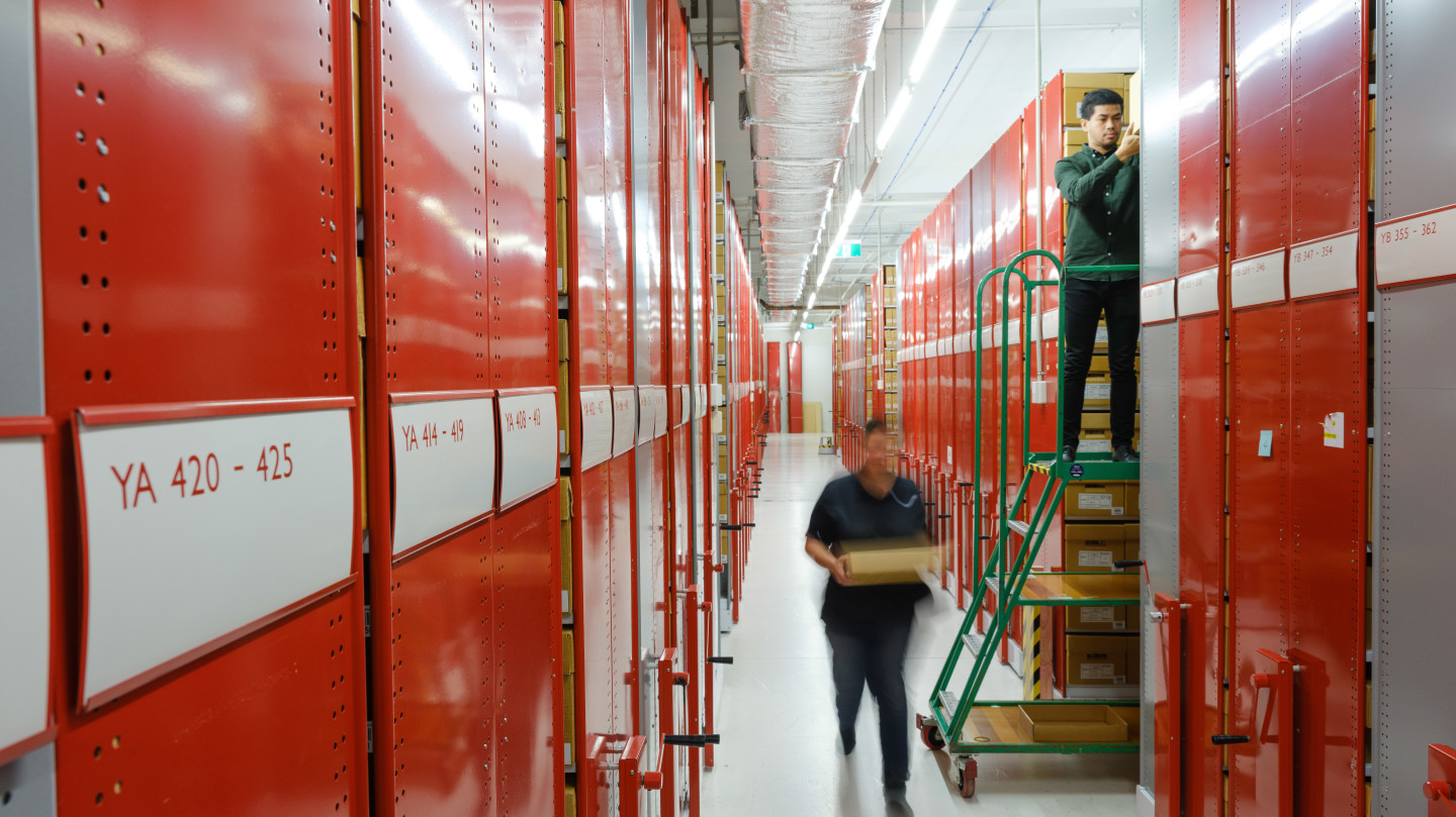 People retrieving cardboard boxes from ceiling height shelves
