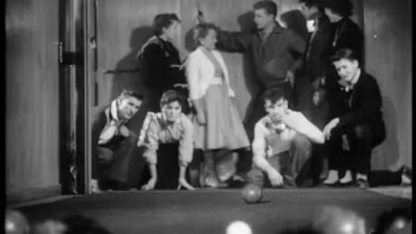A still from 'Pictorial Parade No. 79'. A group of teens play bowls. Crouched on the floor, they watch the ball intently as it rolls.