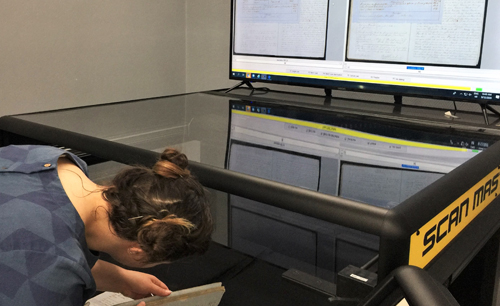 Digitisation Assistant Ish Doney scans a British Consul Deed on the oversize capture machine. Digitisation Assistant Ish Doney is bending down in preparation to scana British Consul Deed on the oversize capture machine.
