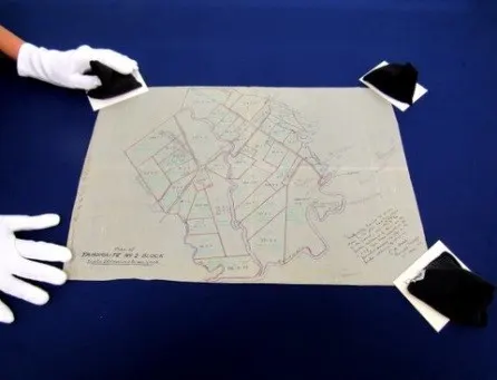 An old map with black weights kept at three corners, one had with white gloves holding one weight and the other hand holding the last corner.