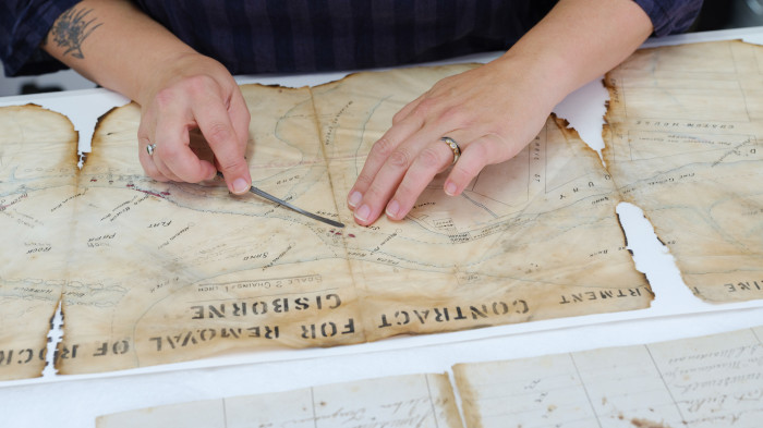 Hands scraping damaged material off an old map