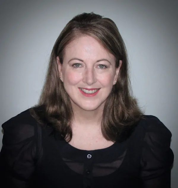 A closeup photo of smiling woman with shoulder length brown hair and wearing a black dress.