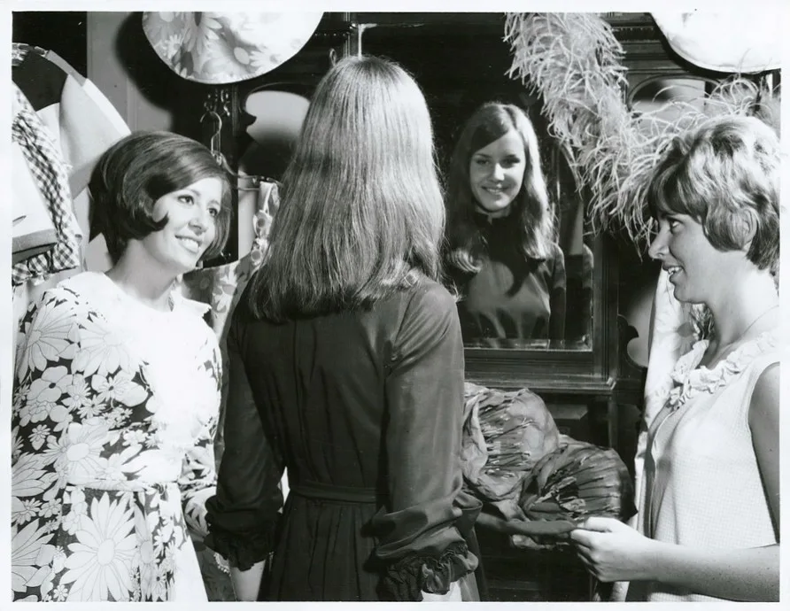 black and white photograph of girls standing around a mirror