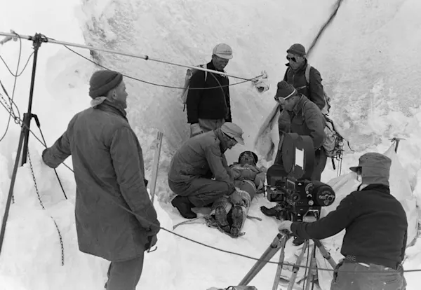 Black and white of few men wearing jackets and hats on a snow mountain.
