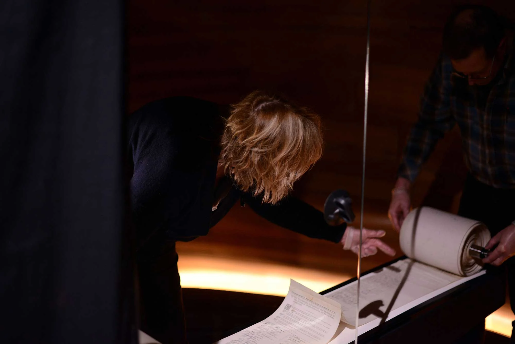 A woman with blonde hair bending and pointing towards a roll of paper.