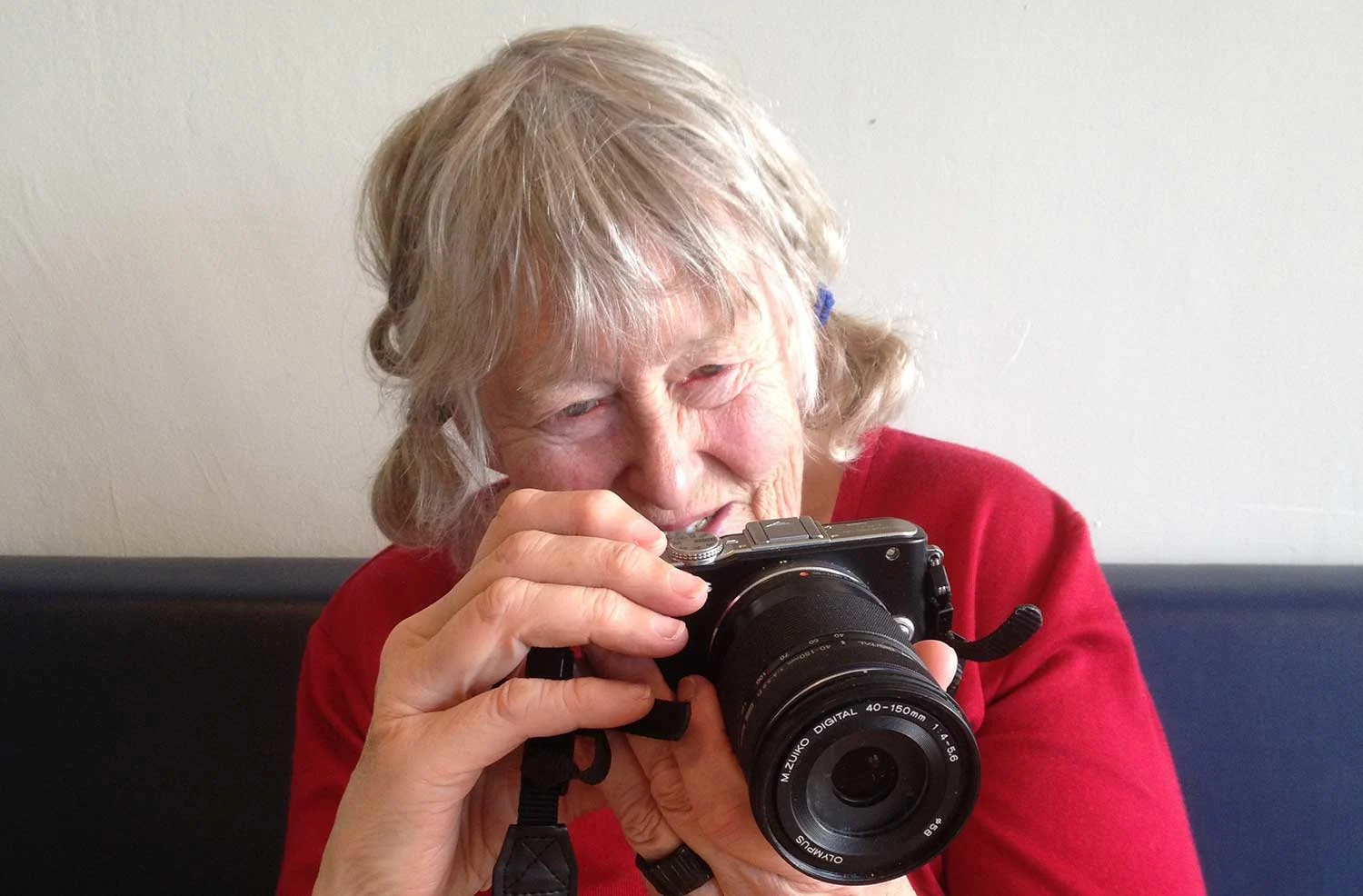 An old woman wearing white white hair, wearing a red shirt holds a lens camera in her hands