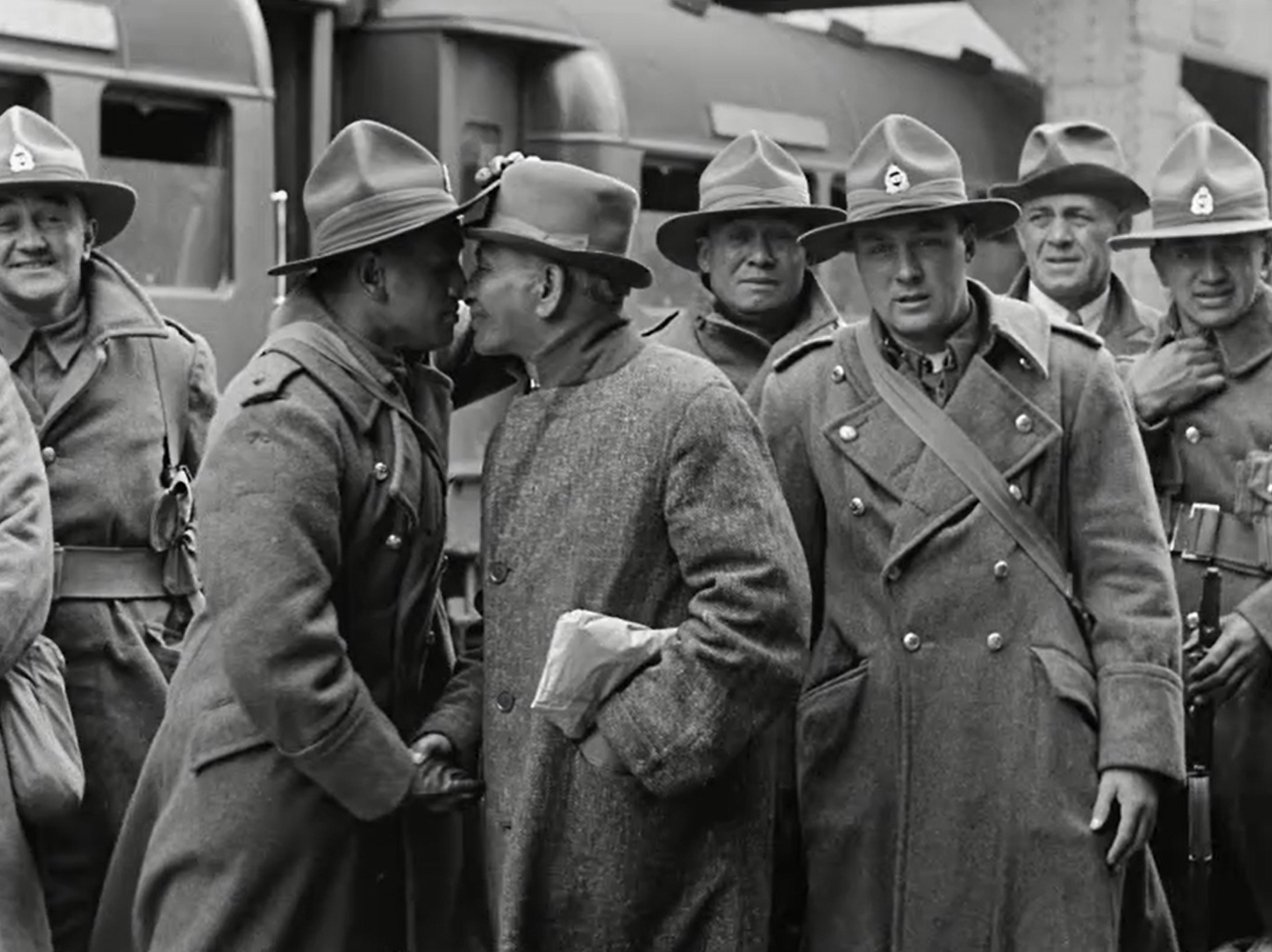 Black and white image of New Zealand troops in front of a train. Two men press their noses together in hongi.