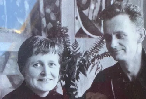 Black and white photo of a smiling woman with short hair and a man standing near her looking at her