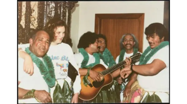 A group of performers gather around a guitar.