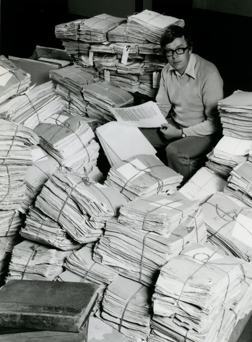 A man sitting surrounded by stacks of papers