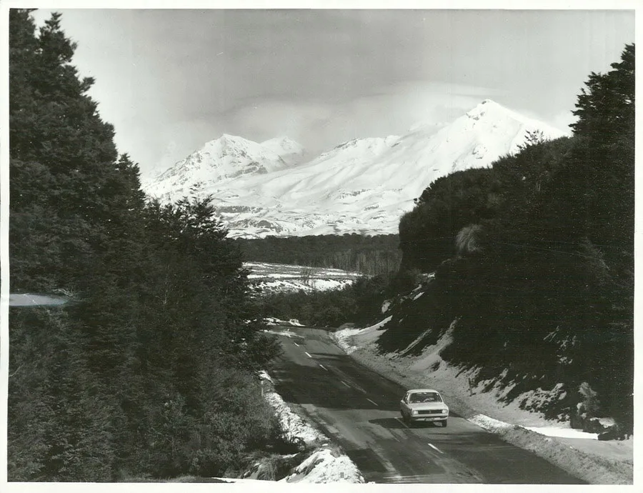 A car driving on a road, mountains on both sides and a snow clad mountain in the background