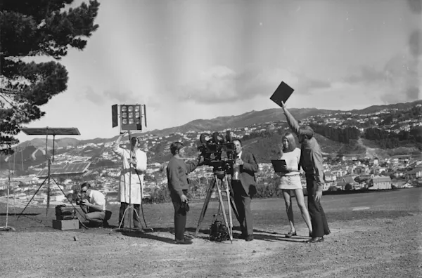 One man crouching, Man with lab coat holding lights, 2 men standinf by a camera and 1 man on the right holding a clapper board.