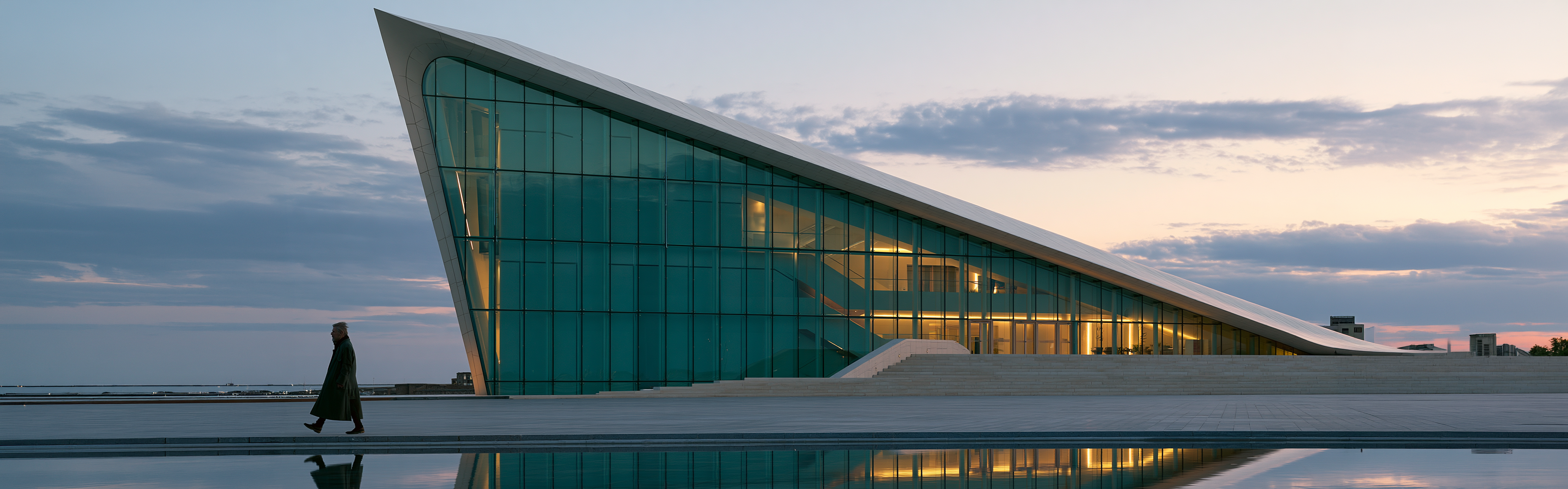 Edificio futuristico in vetro e marmo con una persona in silhouette che cammina sul piazzale antistante al tramonto.