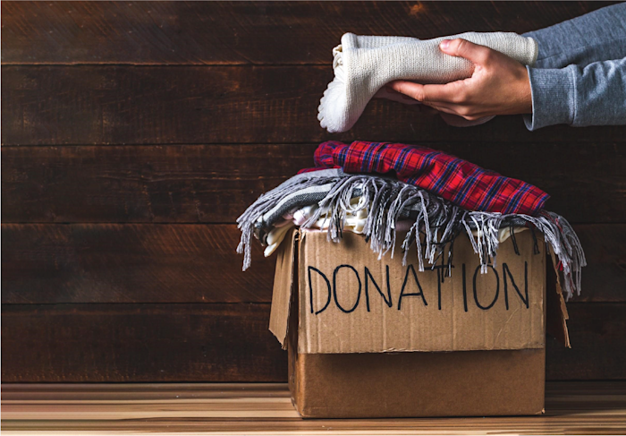 Person placing clothing in a cardboard donation box.