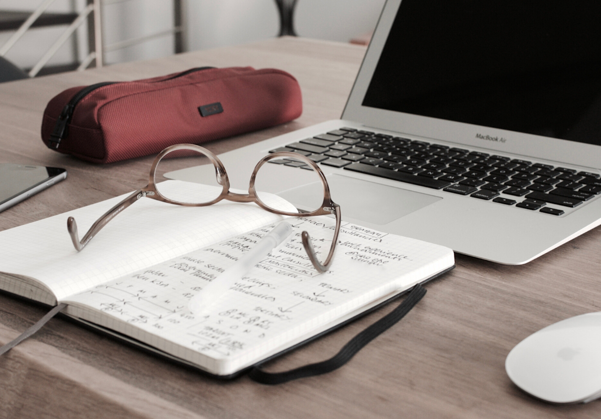Desk with open laptop, notebook and eyeglasses