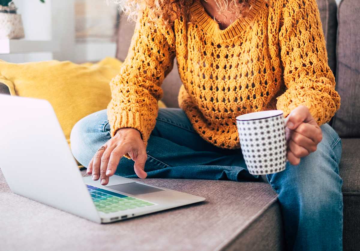 Woman sitting in on the couch working from home holding a mug.