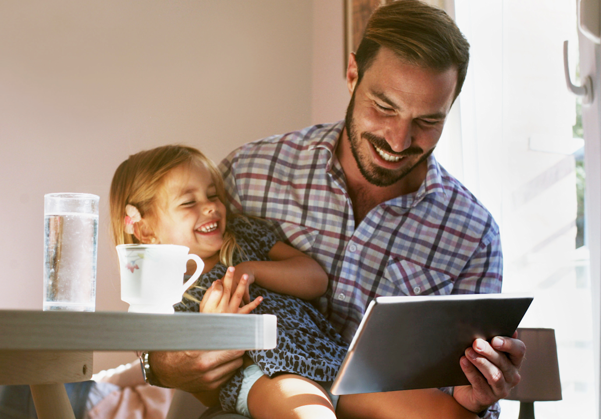 Parent sitting at a table holding child with tablet