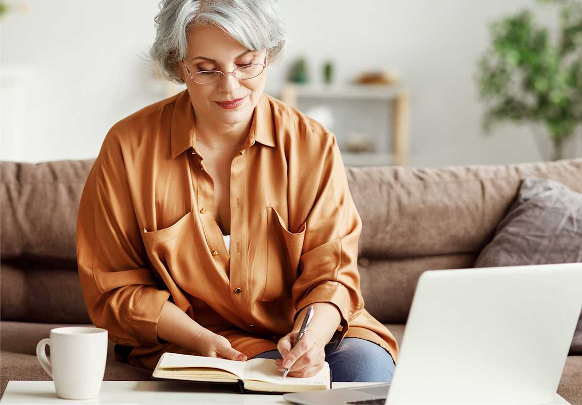 Person sitting on couch taking notes in front of a laptop