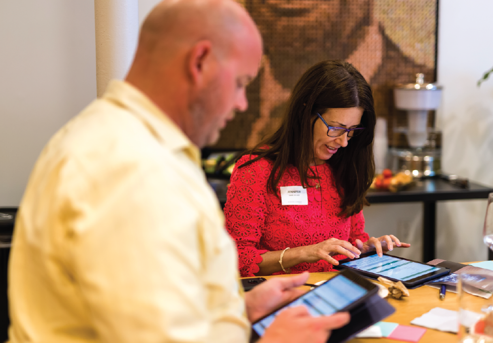 Man and woman sitting at a table participating in an interactive activity on iPads.