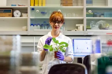 A smiling female plant scientist in a laboratory from RBG Kew, holding a small plant in her hand