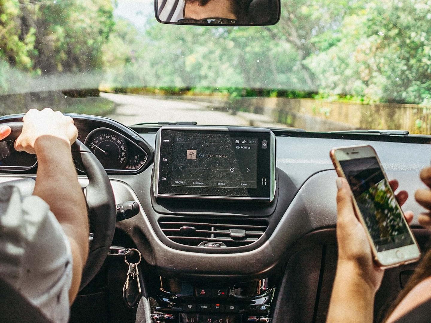Image from behind of person driving with passenger using a phone