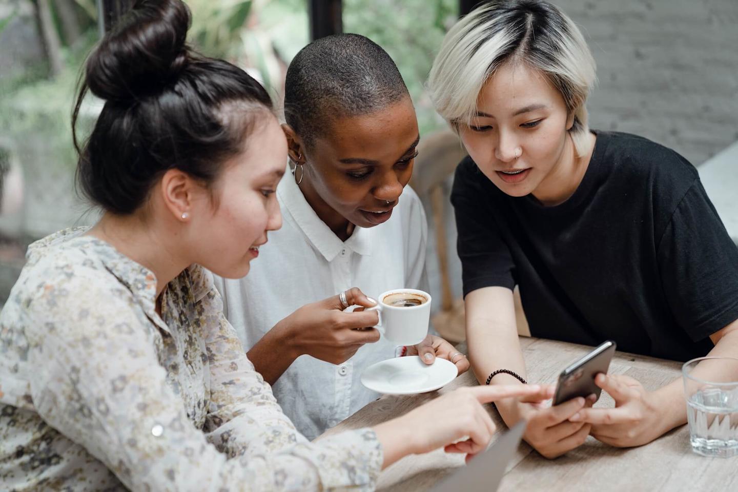3 women drinking coffee and looking at a phone