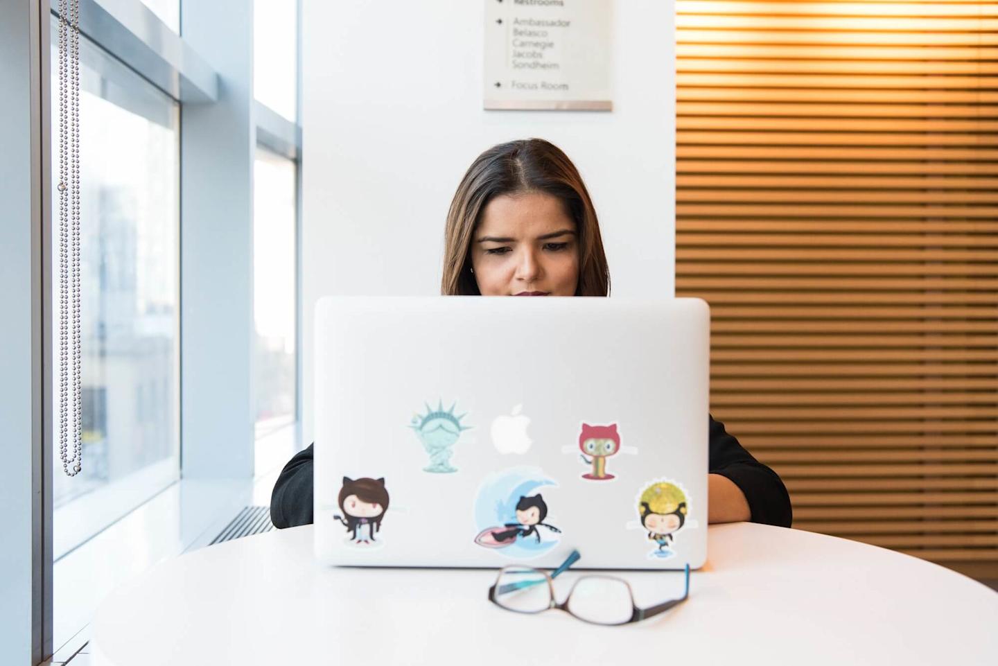 Programmer behind a laptop with many different github stickers on it