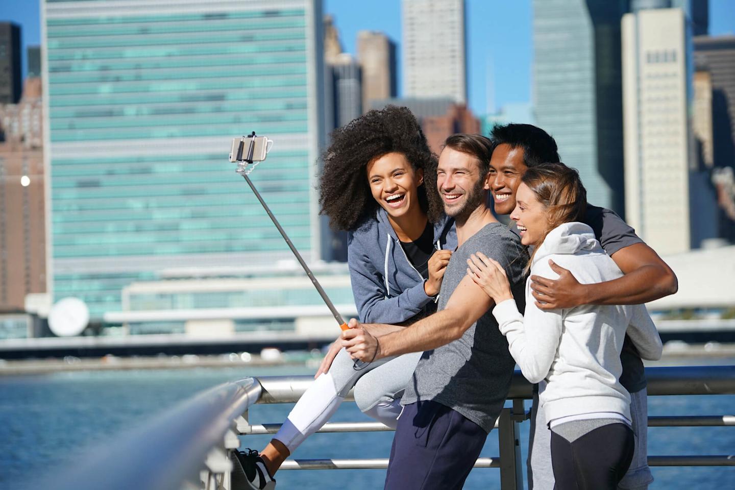 Image of a group of friends taking a picture with a selfie stick with manhattan behind them.