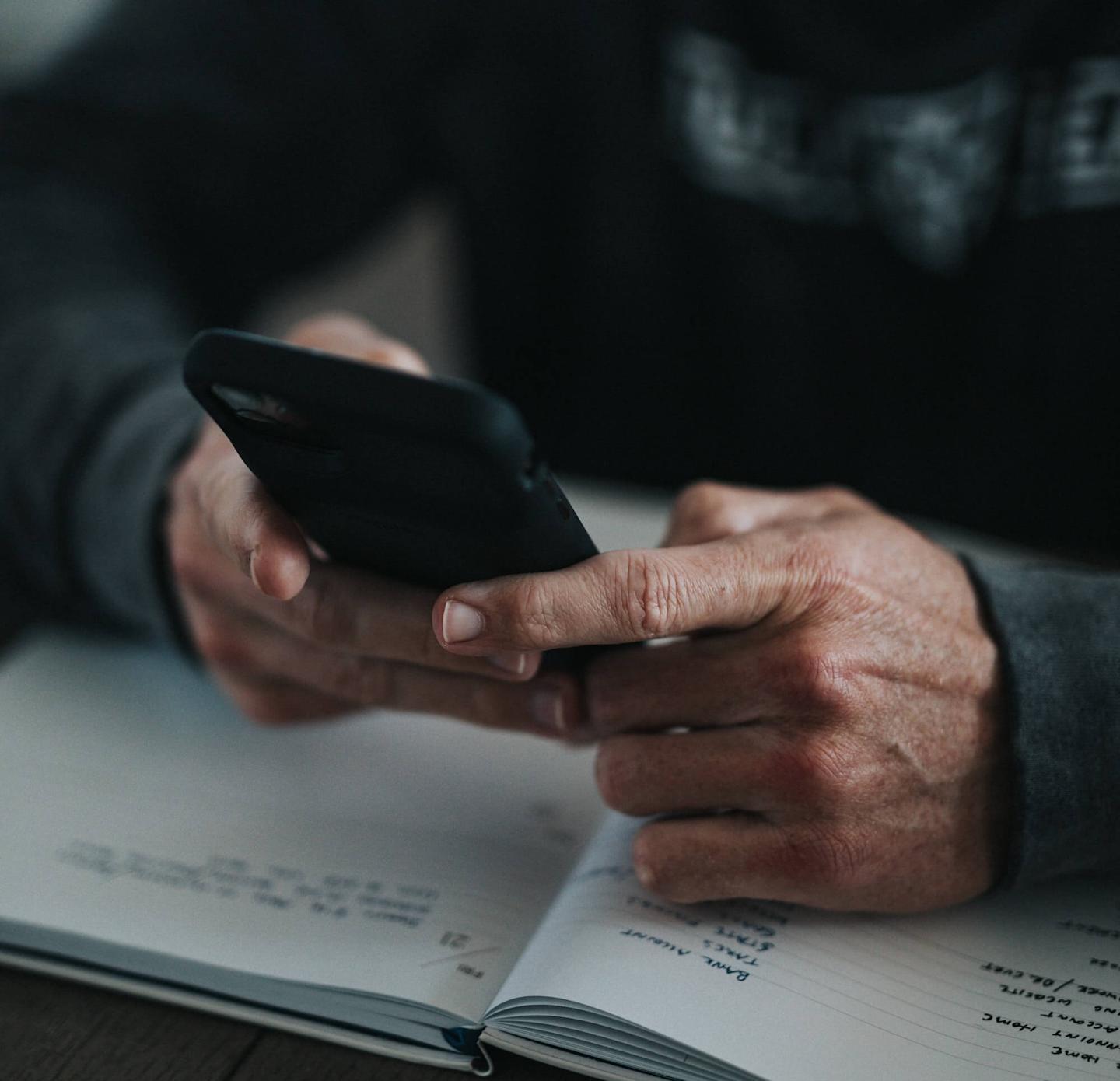 closeup of person using phone on top of a notebook