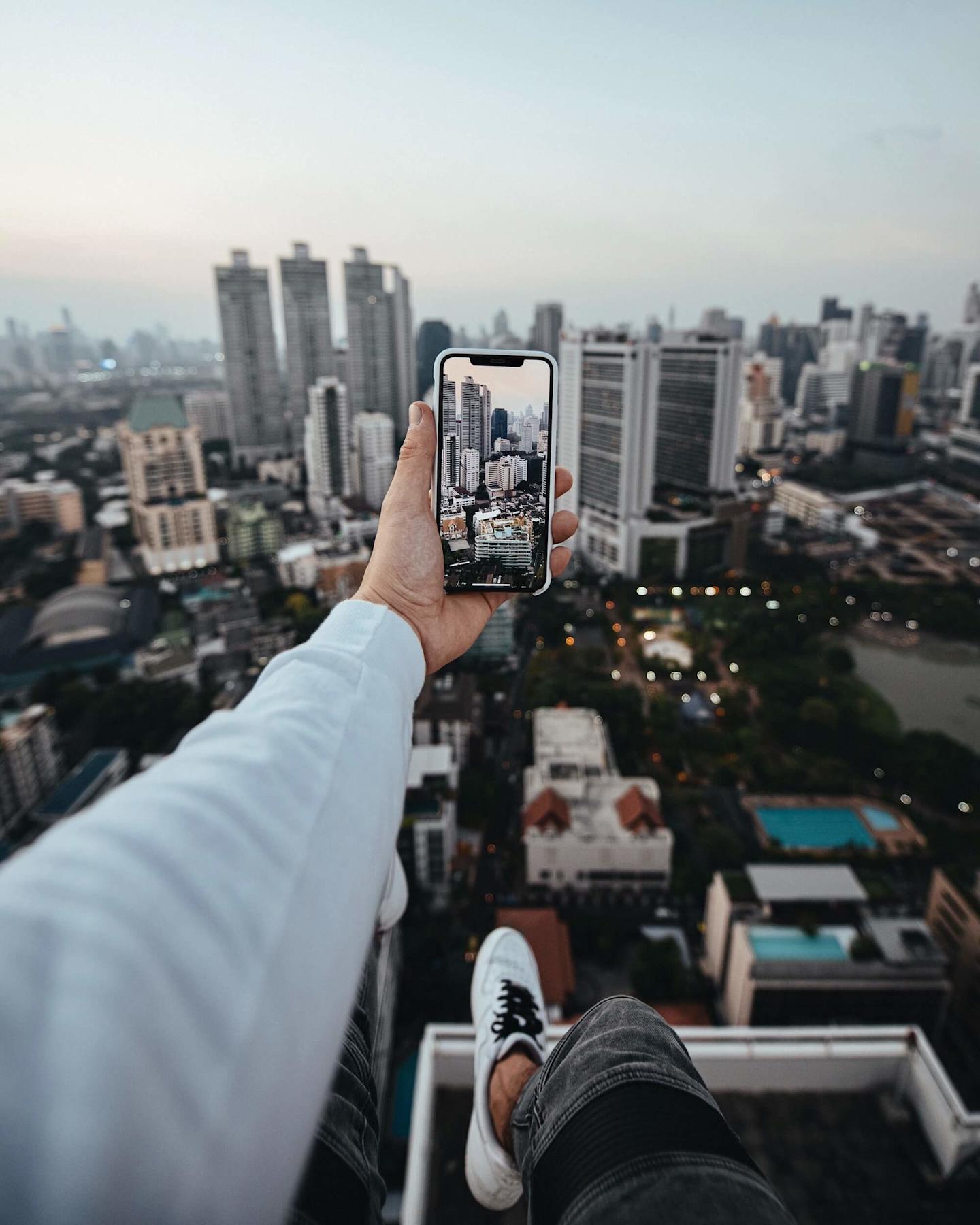 point-of-view image of a person sitting on a tall building taking a photo of other buildings with their phone