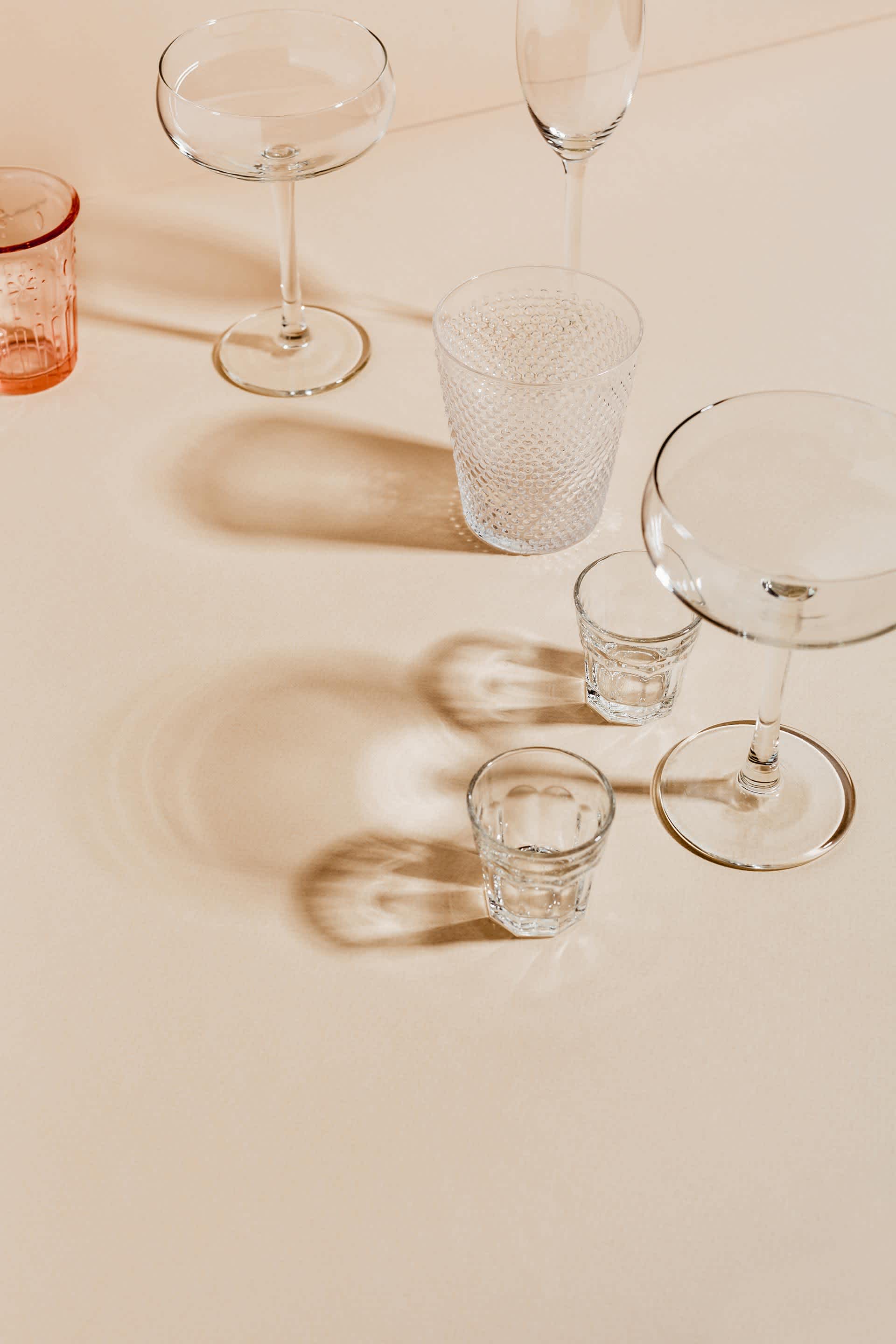 Various sizes and types of drinking glasses on a pink background
