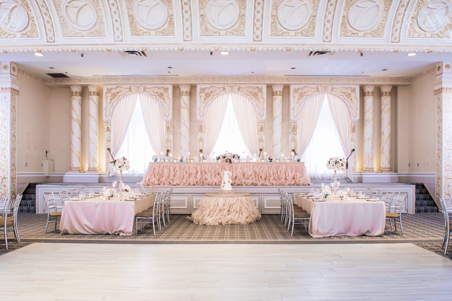 The pink-themed head table at a wedding in a ballroom with a dance floor.