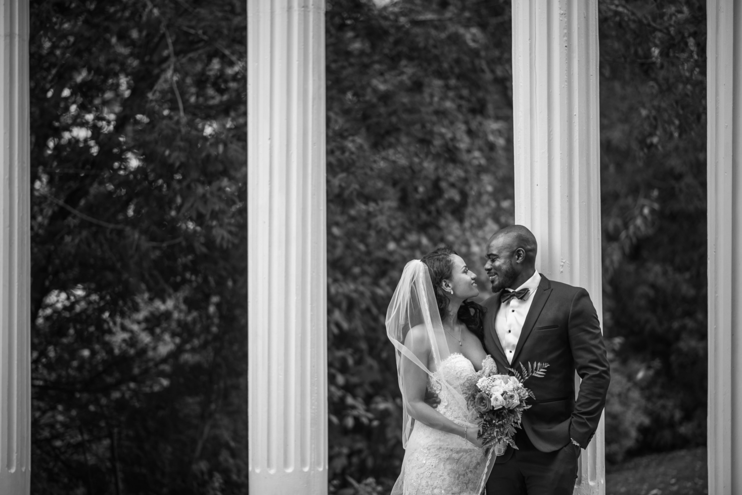 The happy couple, John and Veronica, standing outside, in front of white columns, in a black and white photo.
