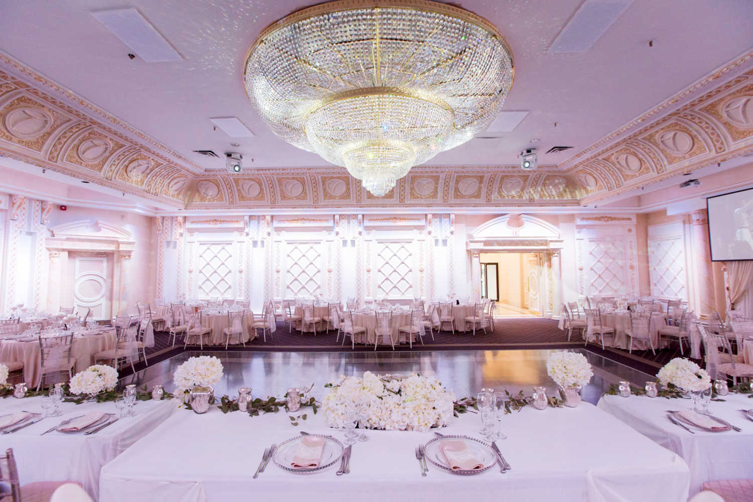 The Queen Victoria Wedding venue at paradise banquet halls with table settings, a large dance floor and a giant chandelier.