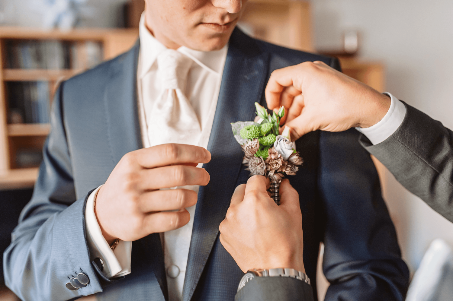 A groom having a flower arrangement attached to their pocket by a helper inside the groom suite at Paradise Banquet Halls.