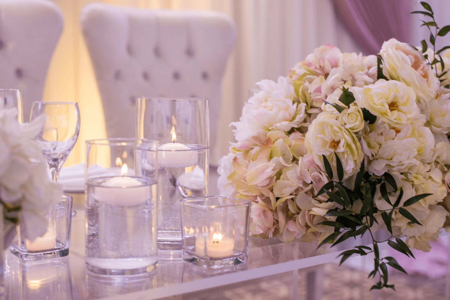 A close-up of a bouquet of flowers at the head table with candles and large, white chairs.