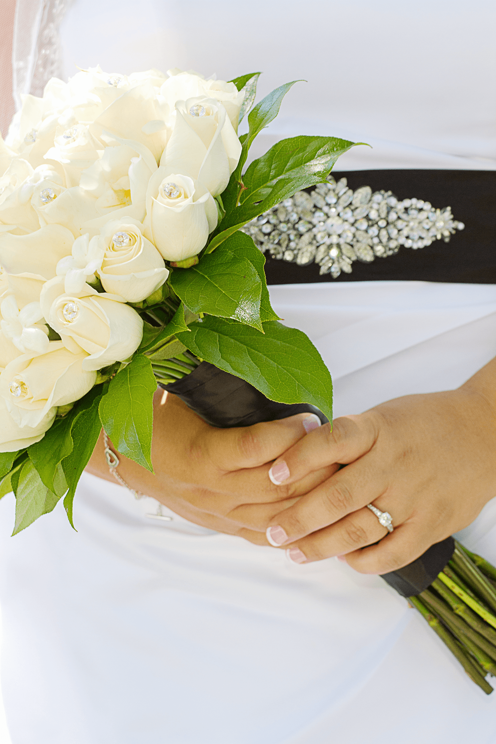 A bride with a bouquet of white roses and a wedding ring on their left hand.
