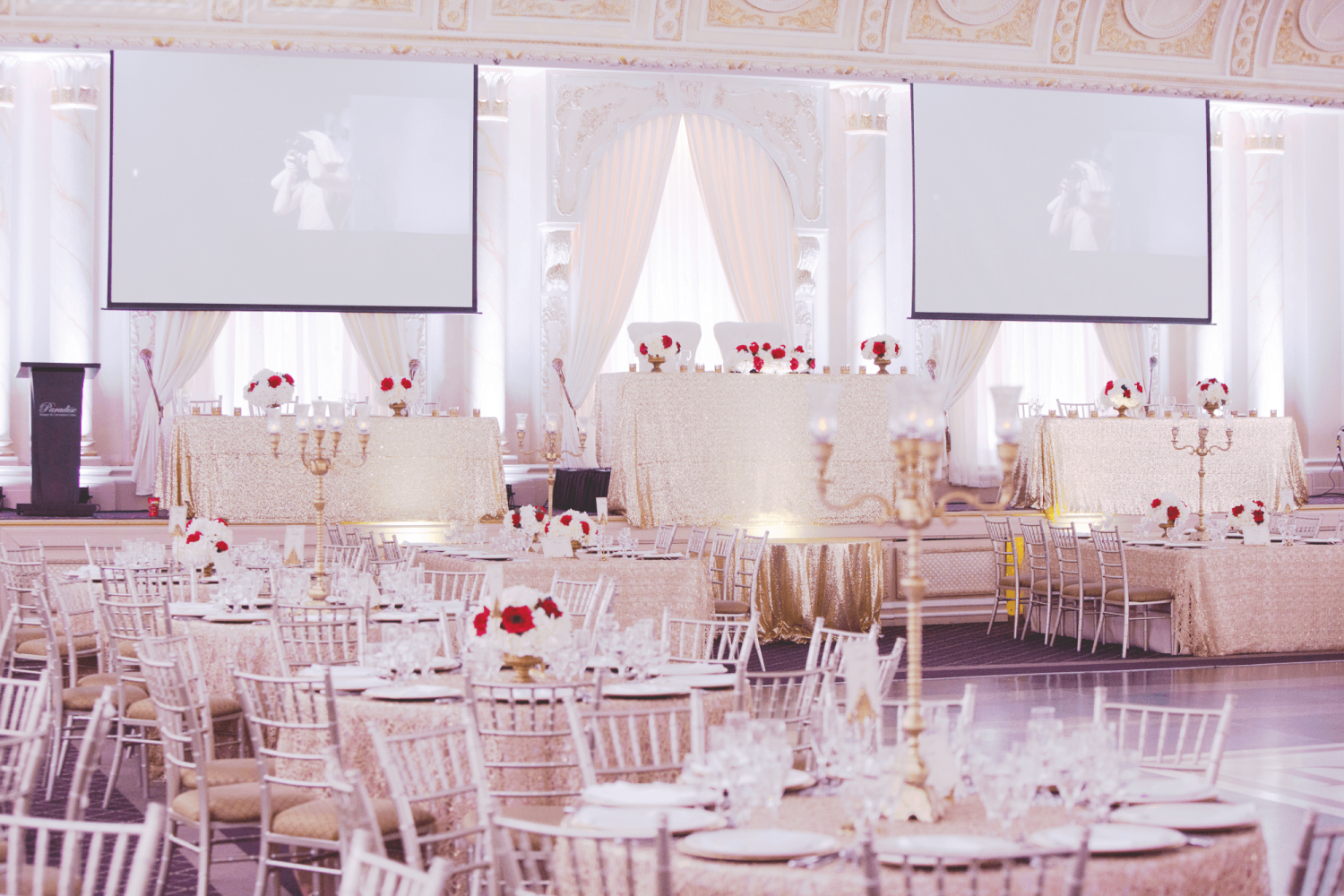 The Queen Mary Ballroom venue at Paradise Banquet Halls with a dance floor, circular tables with chairs, and a raised head table with a red and white flower colour scheme.