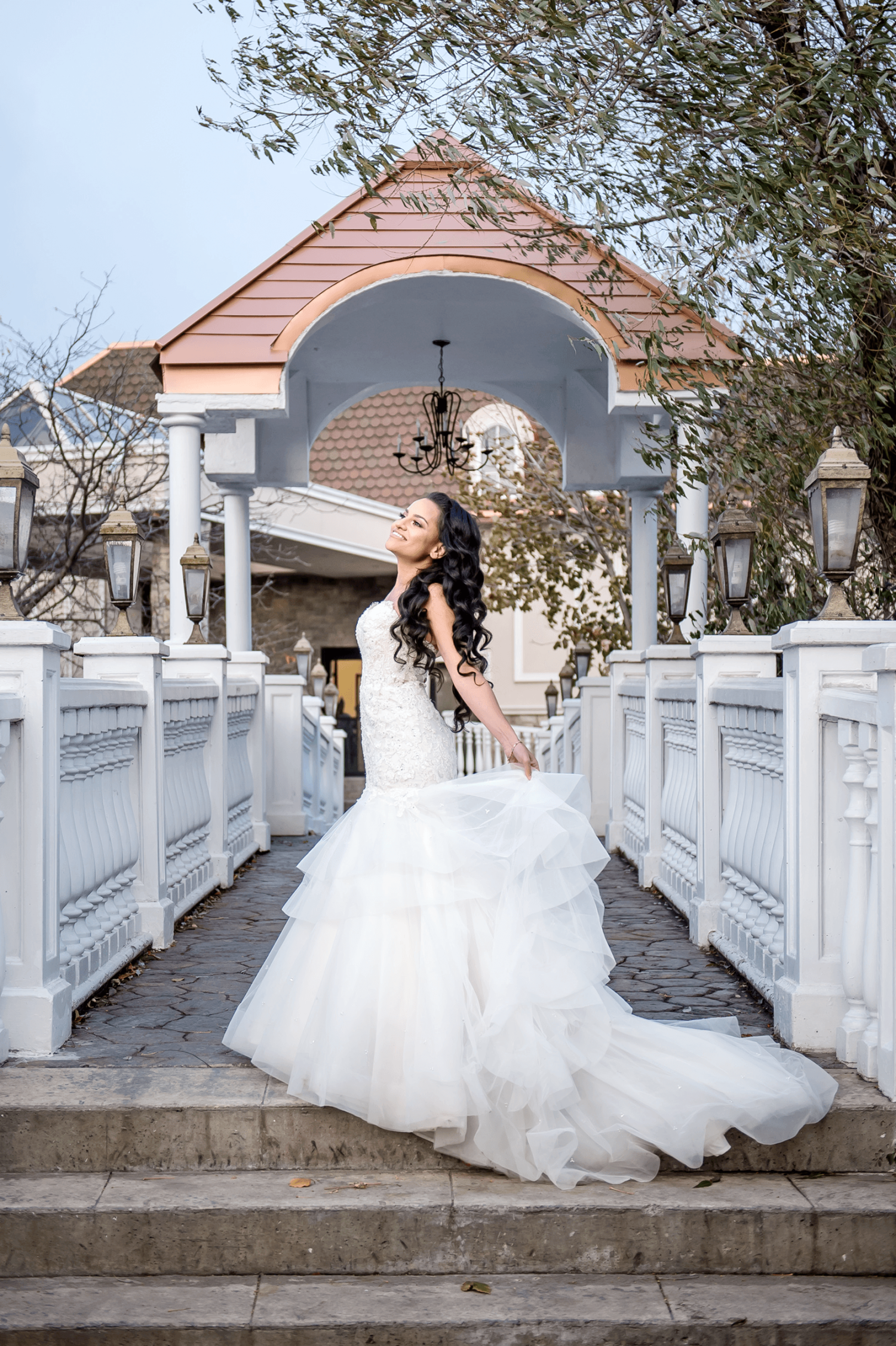 A bride in their wedding dress standing on a bridge with white railing outside at the Paradise Banquet Halls Garden Venue