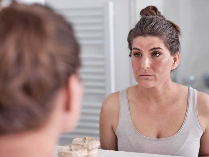 Frau mit Neurodermitis betrachtet sich im Spiegel
